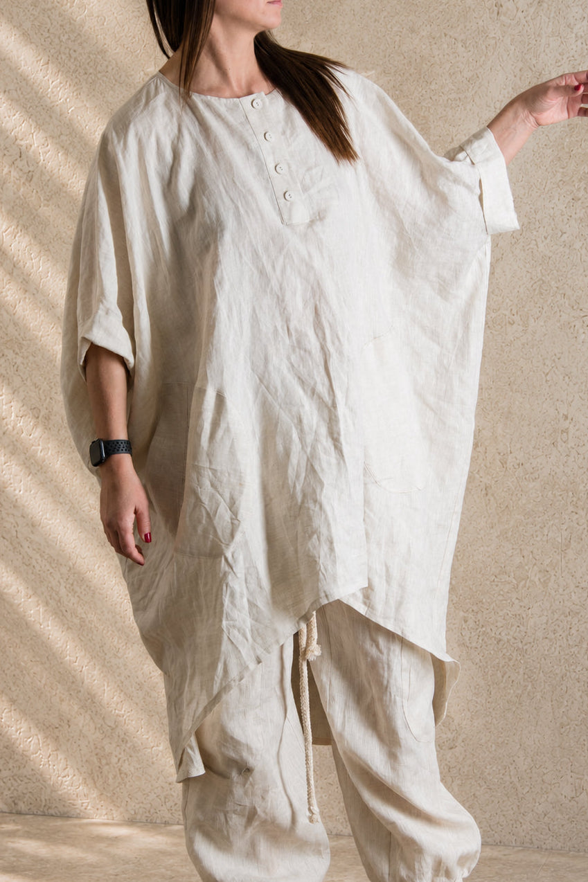 Person wearing a loose-fitting natural linen outfit against a beige wall.