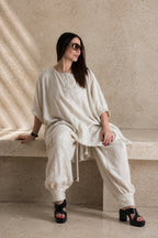 Woman in a natural beige linen outfit sitting on a stone bench with a neutral background
