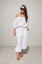 Woman wearing a white outfit with sunglasses against a plain background