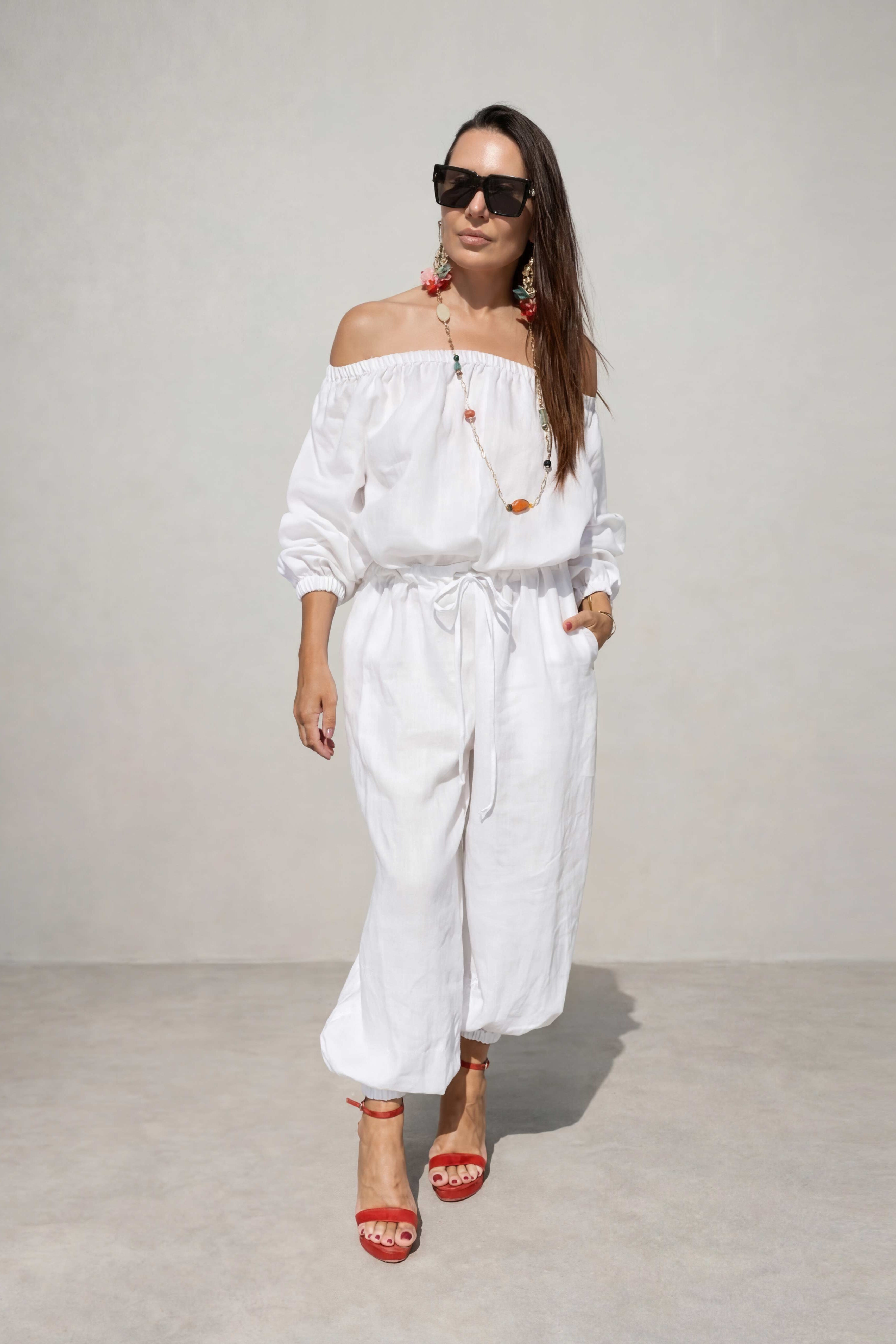 Woman wearing a white outfit with sunglasses against a plain background
