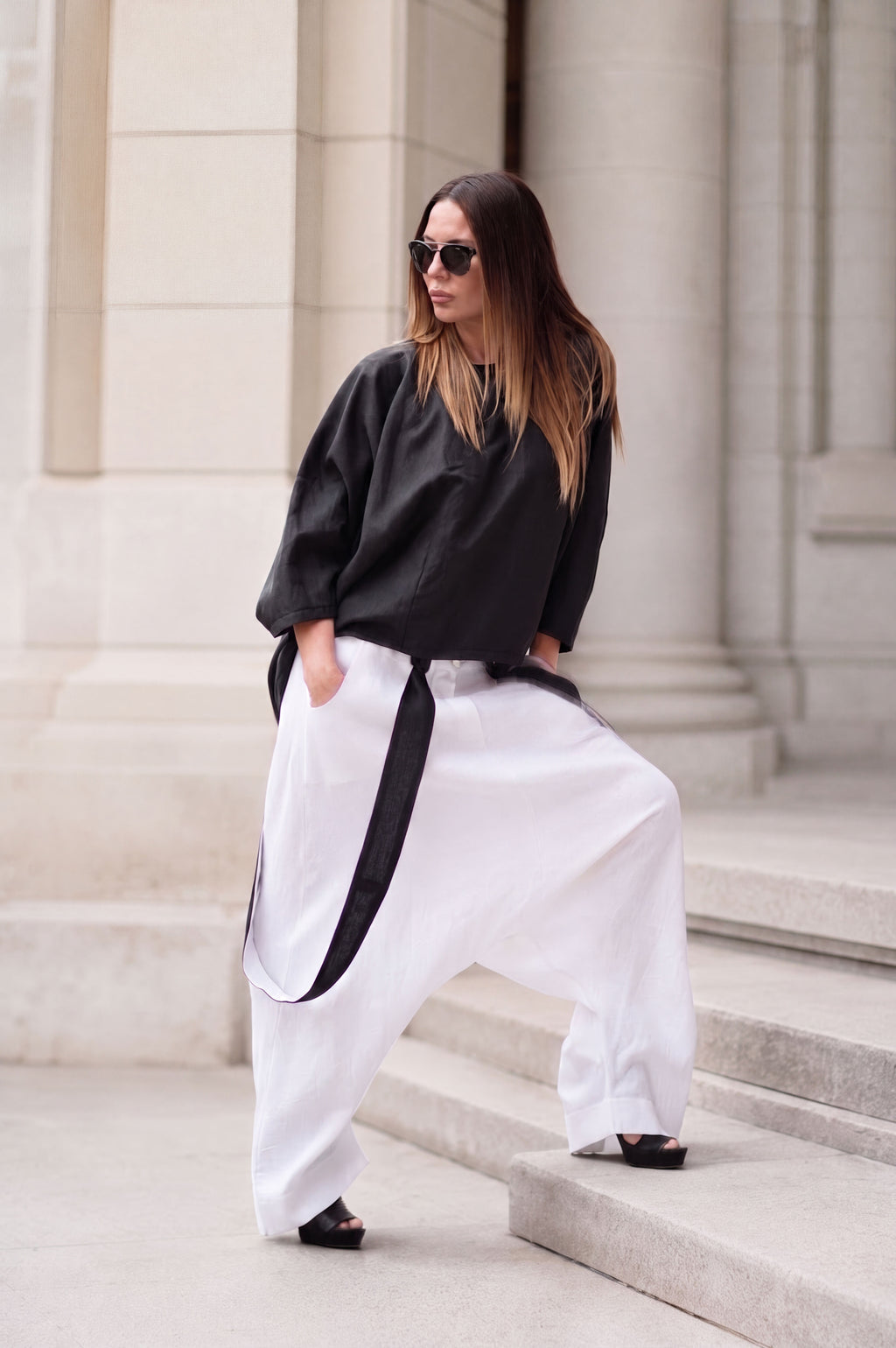 Woman wearing a black top and white linen pants with a belt, standing on stone steps.