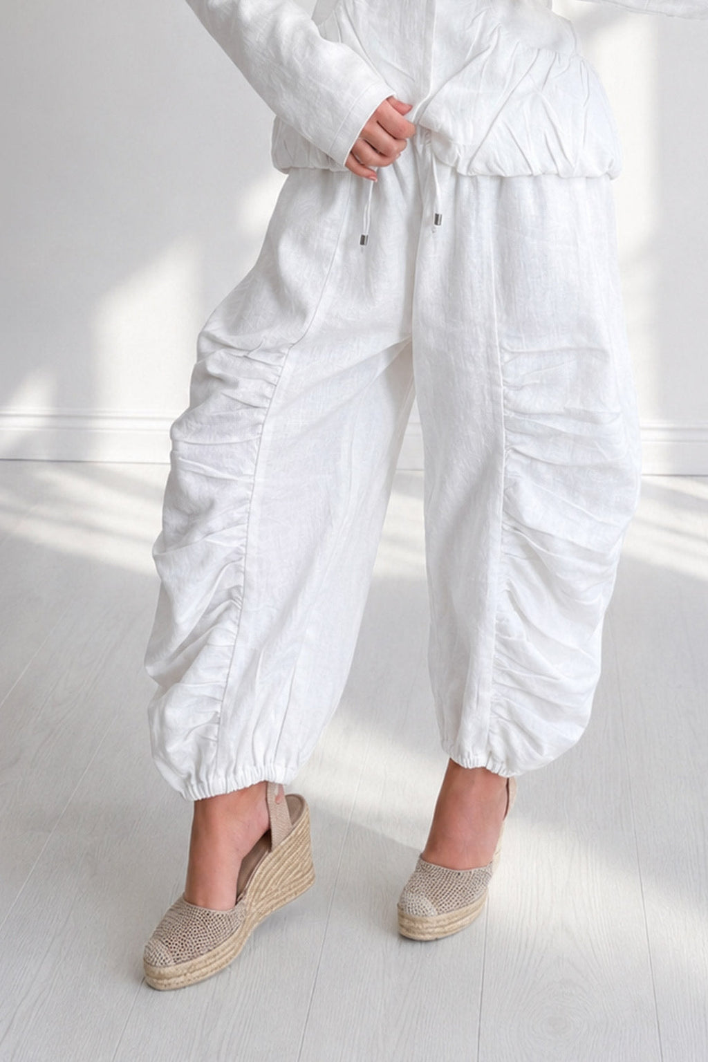 Person wearing a white outfit with wide-leg pants on a light wooden floor.