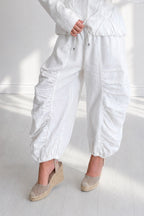 Person wearing a white outfit with wide-leg pants on a light wooden floor.