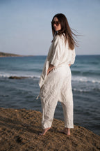 Woman in a white outfit standing on a beach with ocean waves in the background