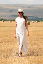 Woman in a white linen dress and hat standing in a field of straw bales.
