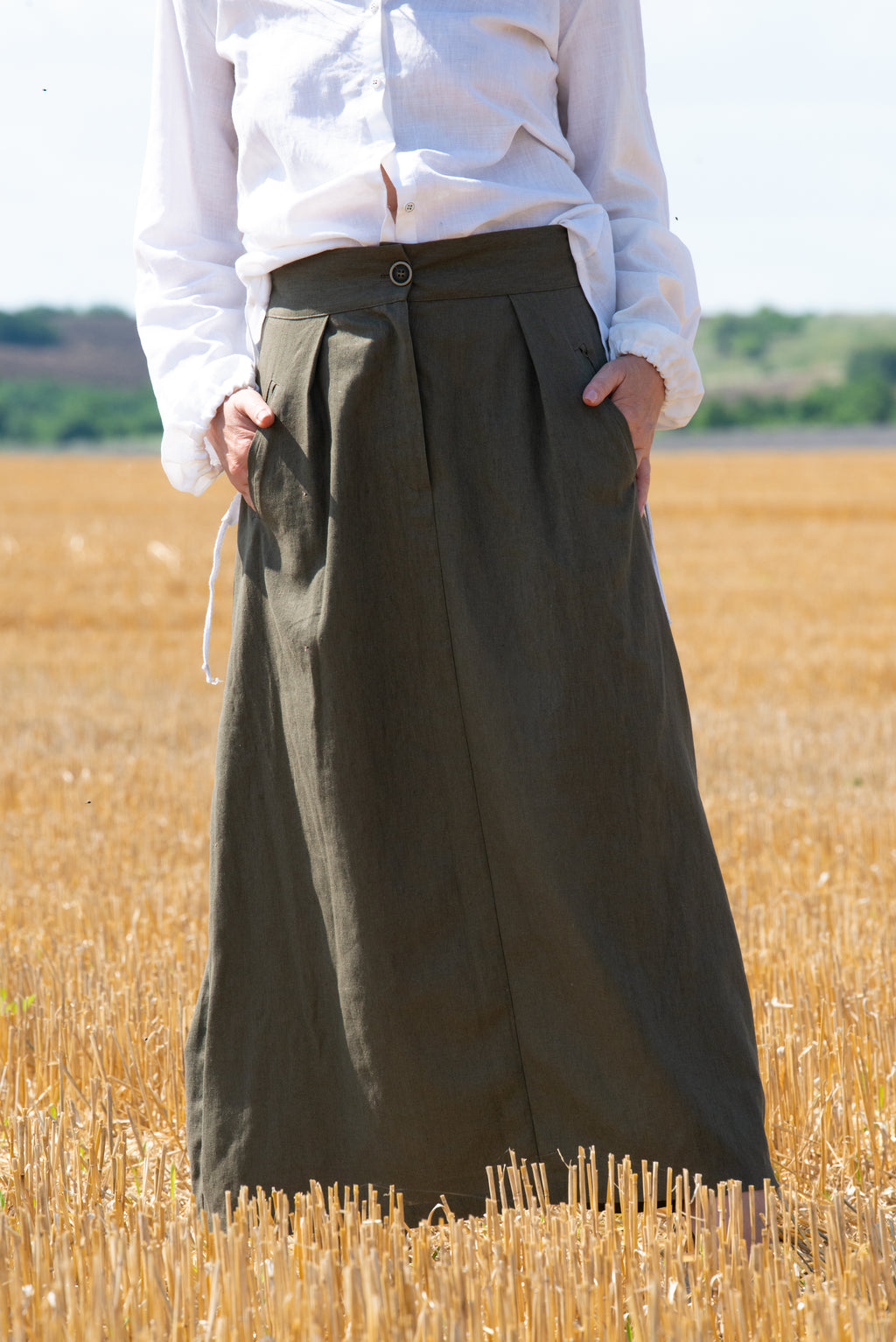Person wearing a long green skirt standing in a field of golden wheat.