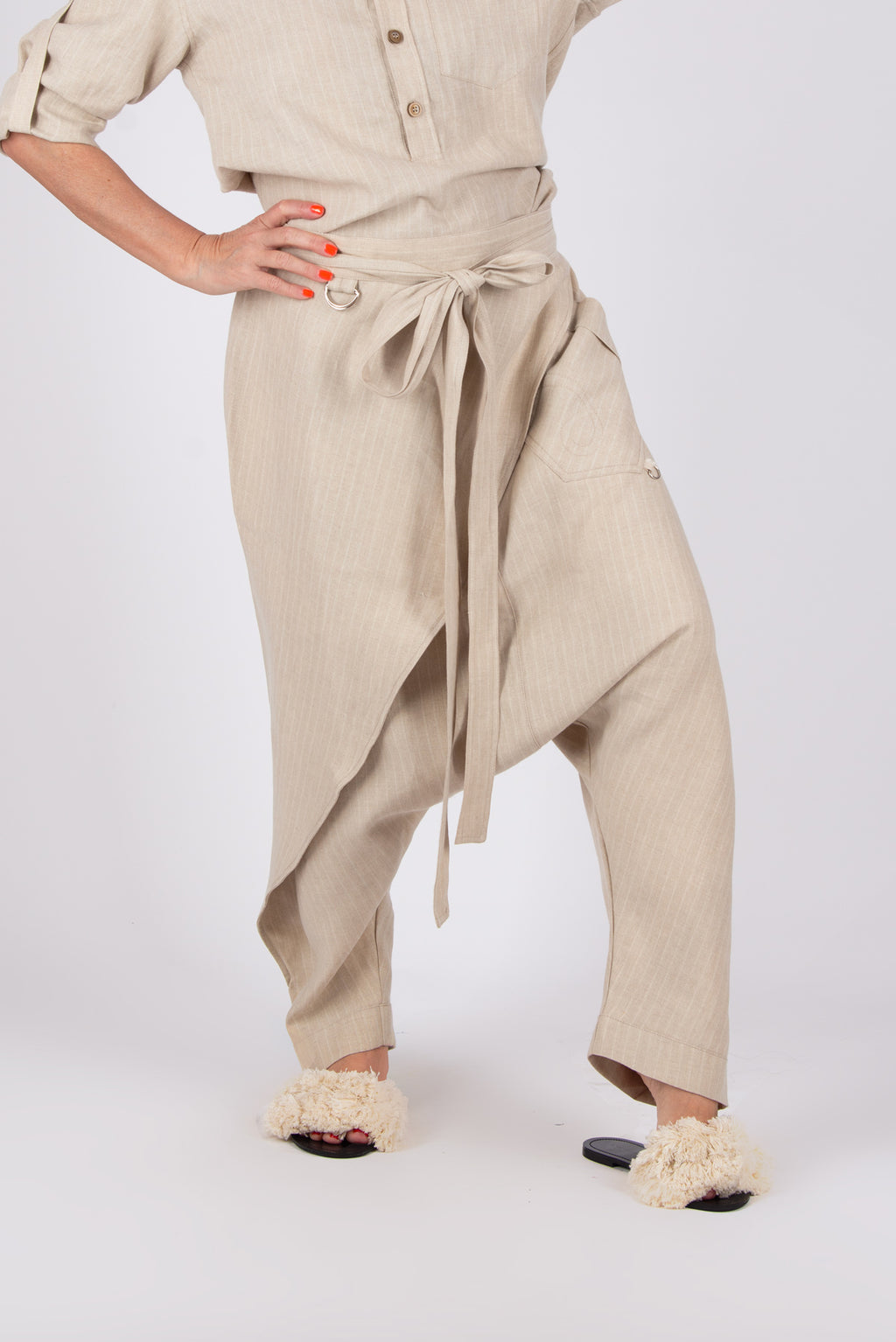 Person wearing a beige linen outfit  pants with a tie-waist pants and shirt on a white background