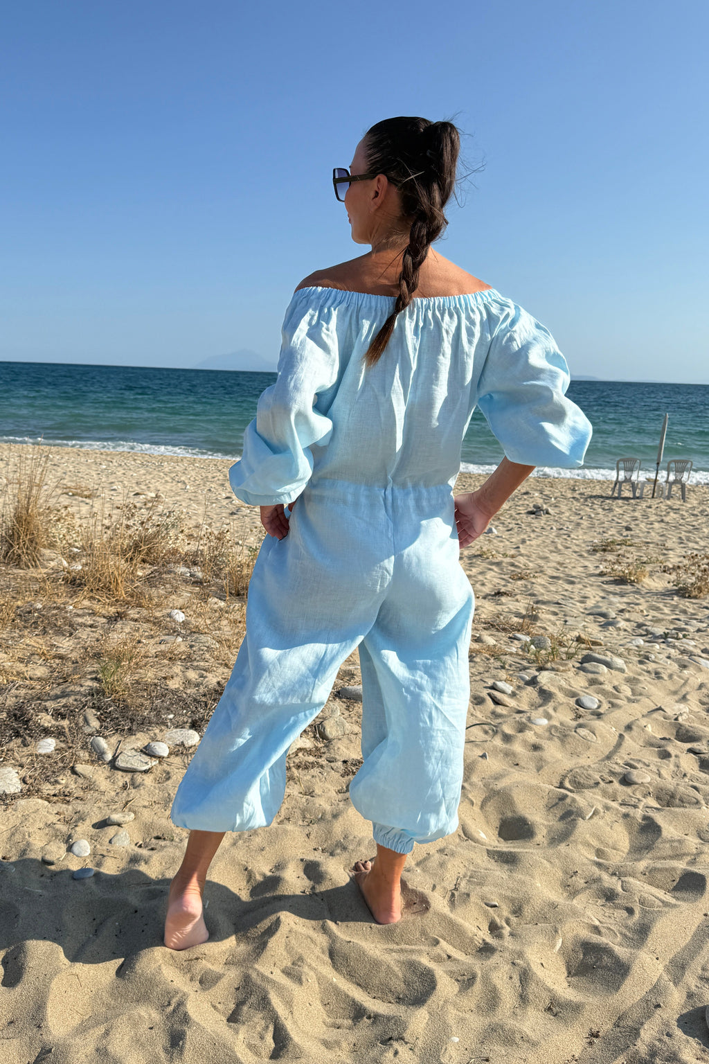 Woman in a light blue outfit standing on a sandy beach with ocean view