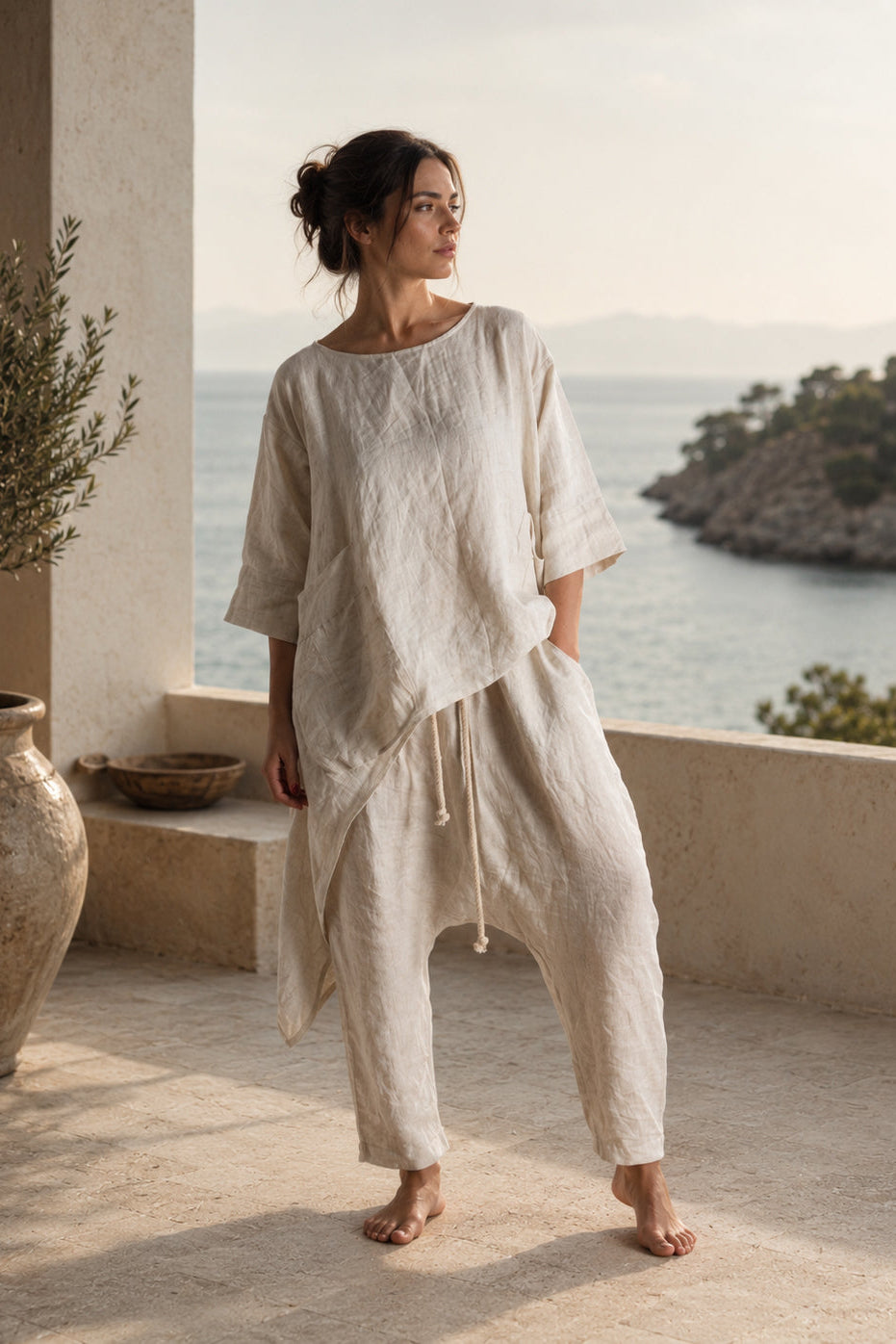 Woman in a light beige outfit standing on a balcony with a scenic view of water and greenery.