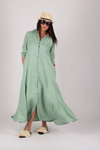 Woman wearing a long mint  linen green dress with a hat and sunglasses on a white background
