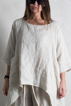 Person wearing a loose-fitting beige linen top and pants against a plain background
