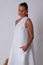 Woman wearing a white sleeveless dress with red earrings against a plain background