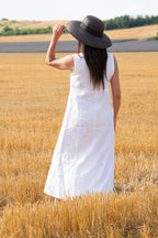 Woman in a white linen dress and straw hat standing in a wheat field.