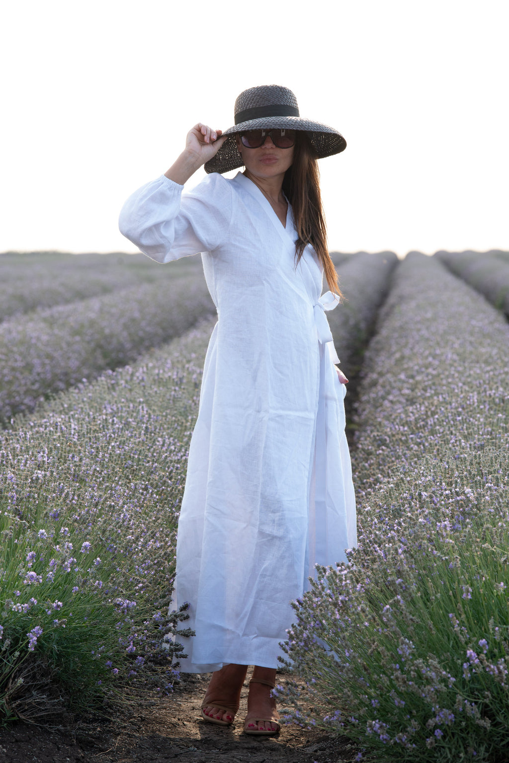 Woman in a white dress and black hat standing in a lavender field.