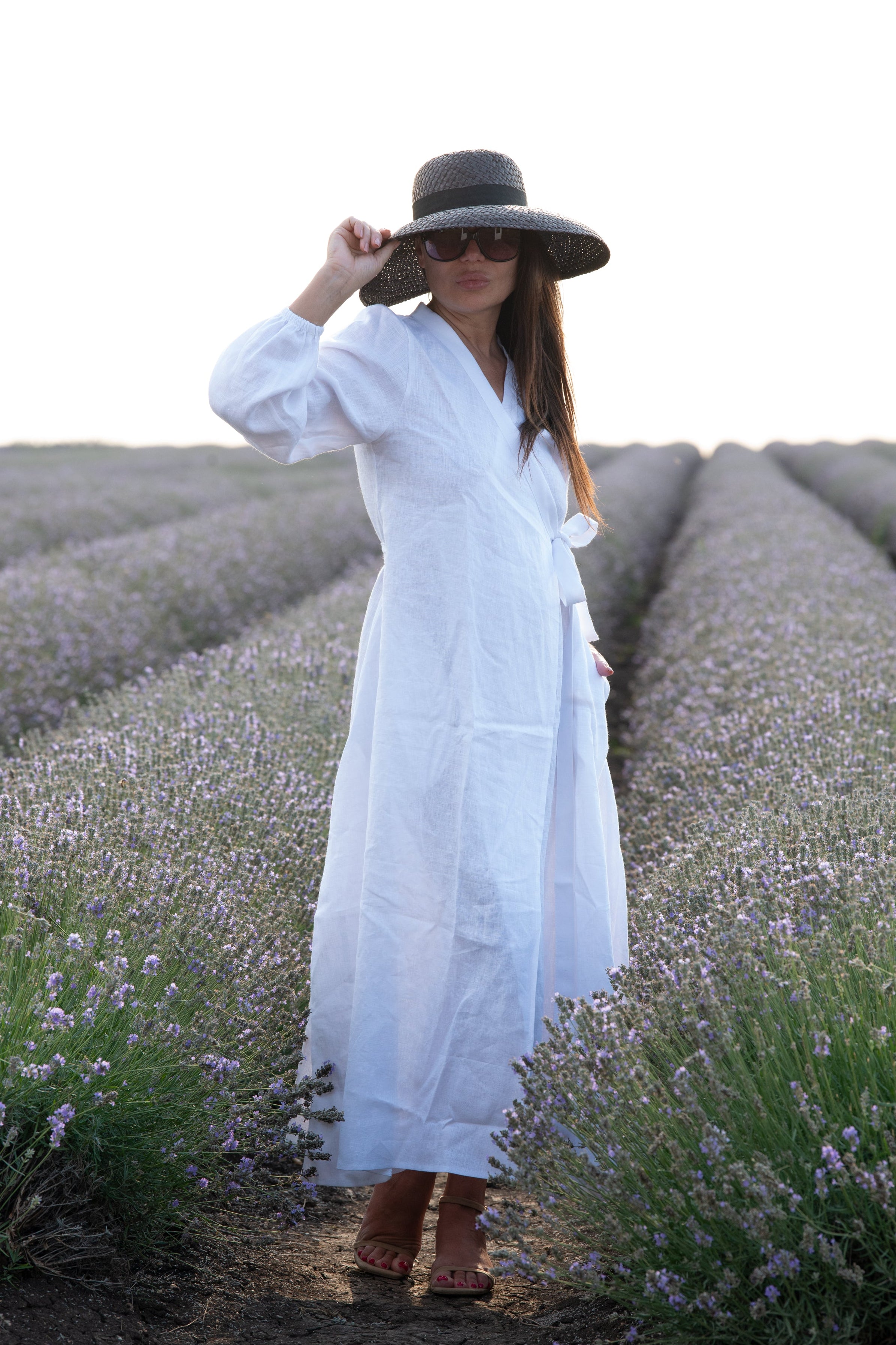 Woman in a white dress and black hat standing in a lavender field.