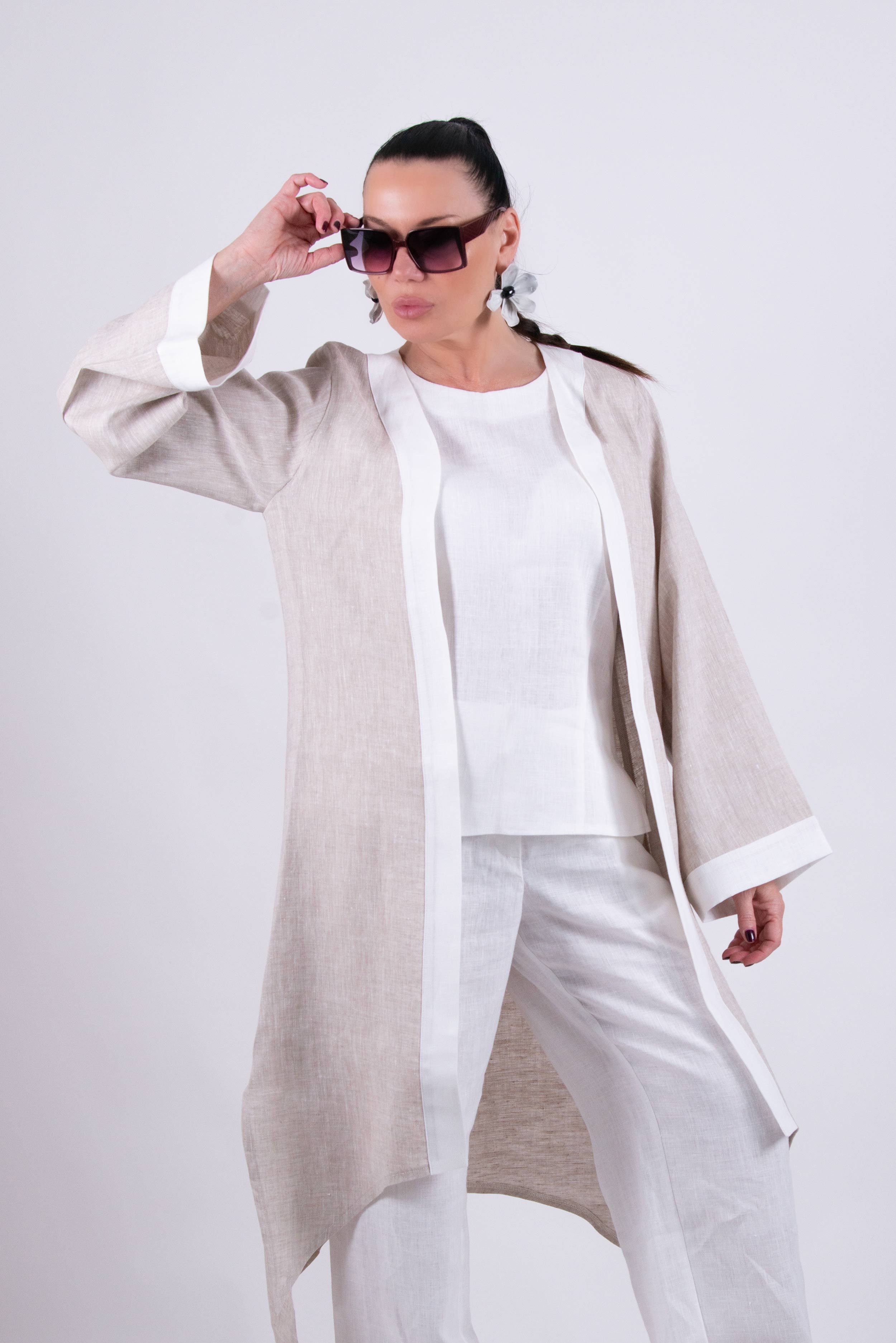 A person wearing a beige and brown two-tone linen duster cardigan with wide sleeves and an open front design, sitting on a white sofa.