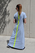 Woman wearing a long light grey dress with a bright yellow stripe on the back