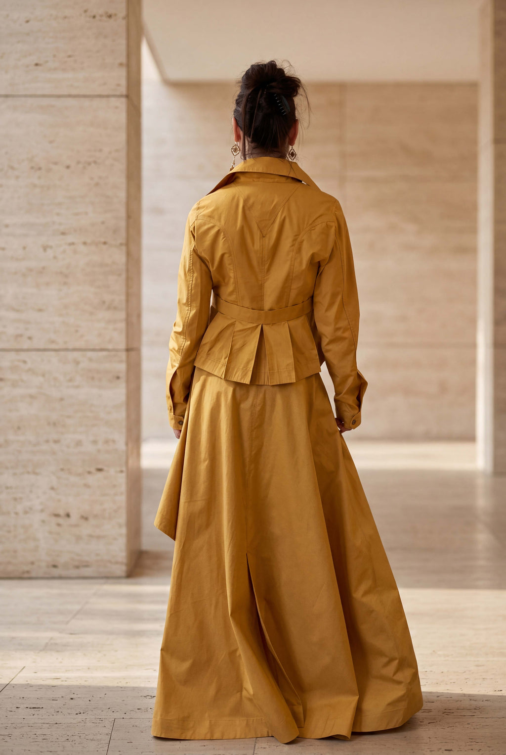 Person wearing a mustard yellow trench coat in an indoor setting with wooden walls.