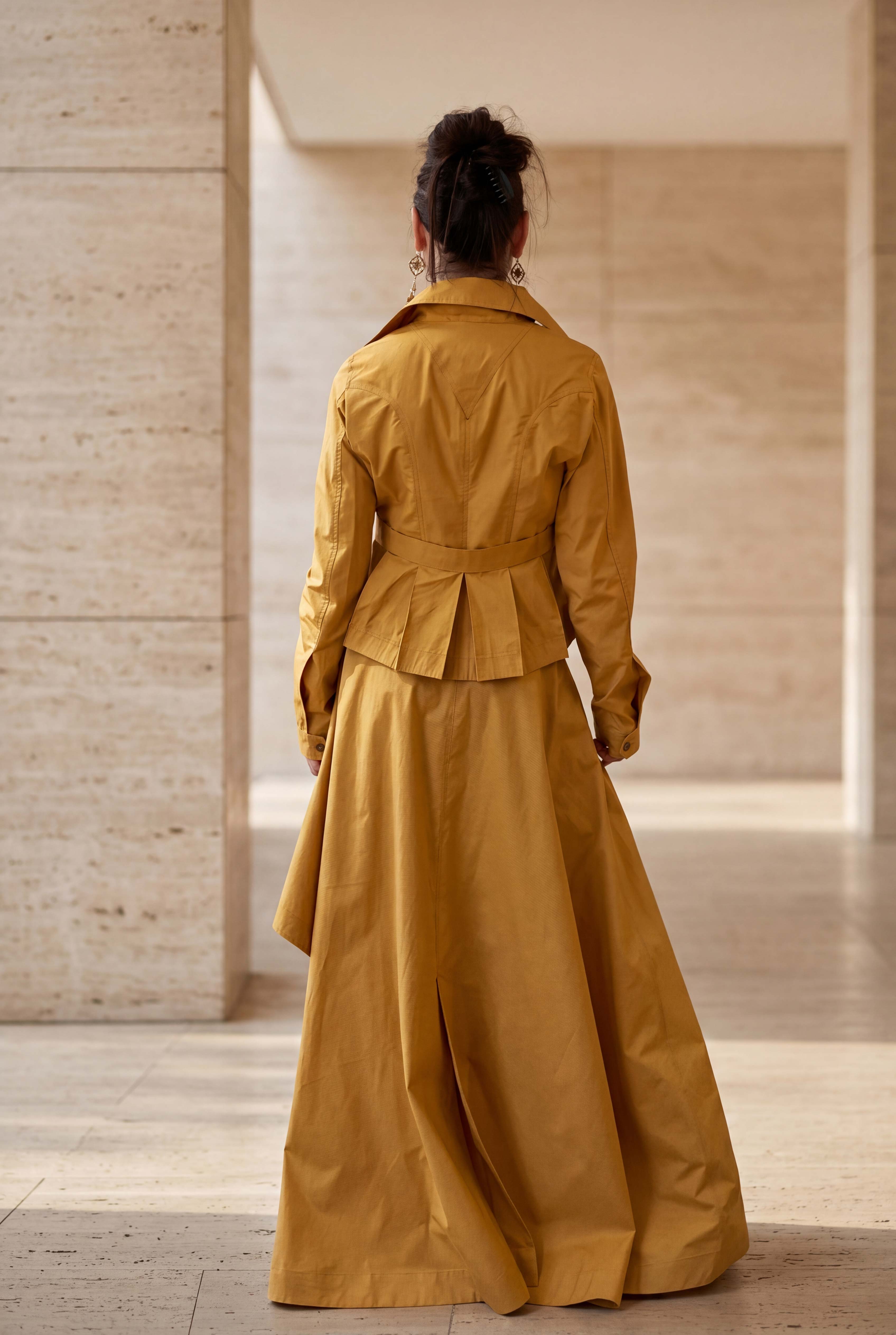 Person wearing a mustard yellow trench coat in an indoor setting with wooden walls.
