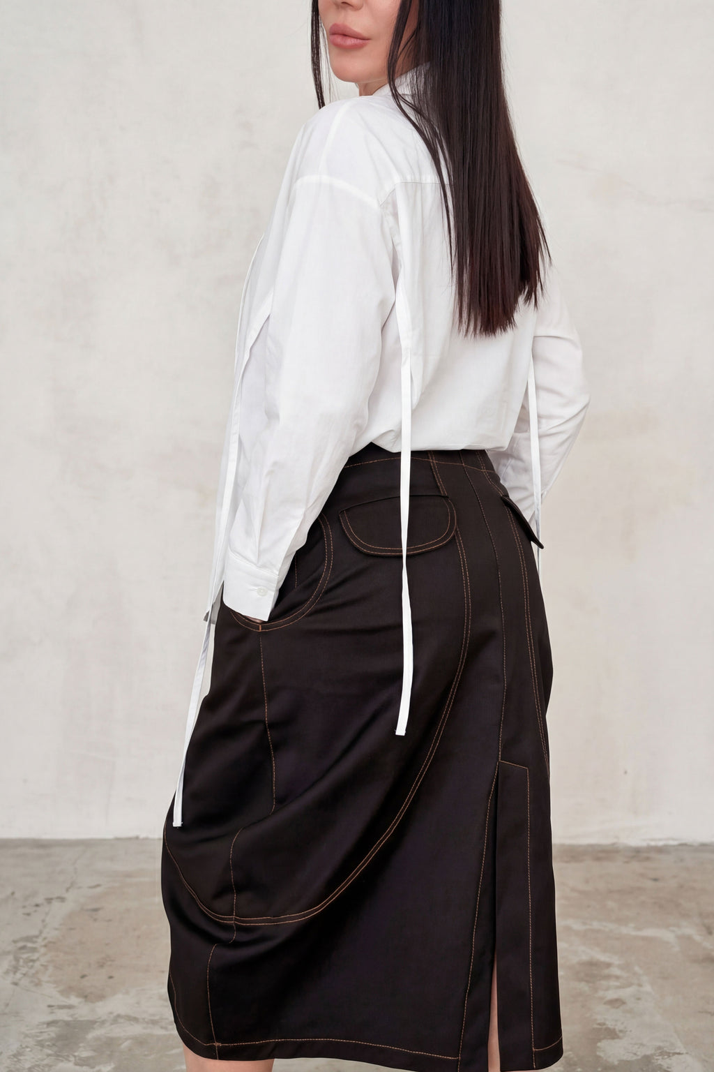 Person wearing a white shirt and brown skirt against a plain background