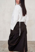 Person wearing a white shirt and brown skirt against a plain background