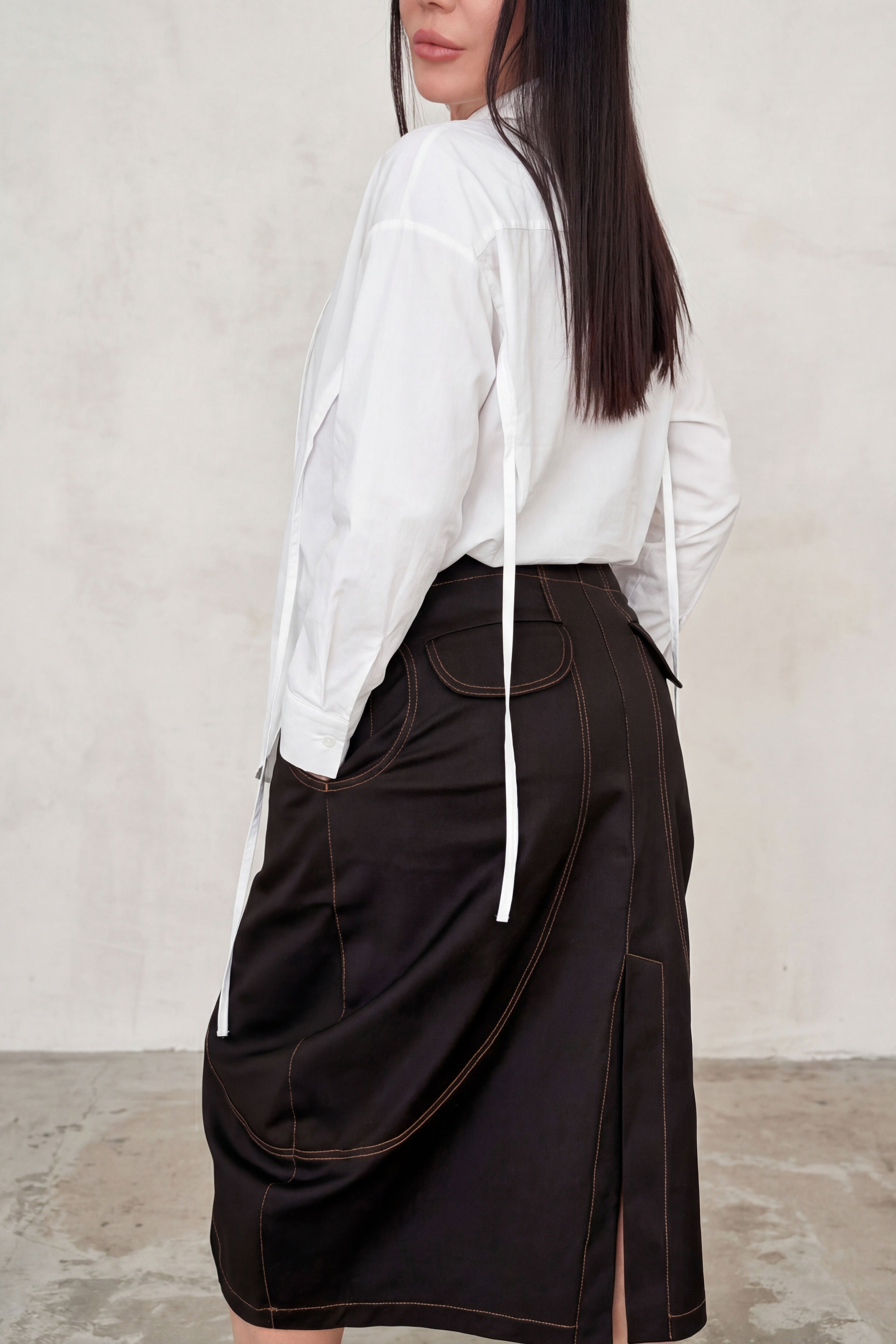 Person wearing a white shirt and brown skirt against a plain background