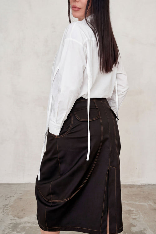Person wearing a white shirt and brown skirt against a plain background