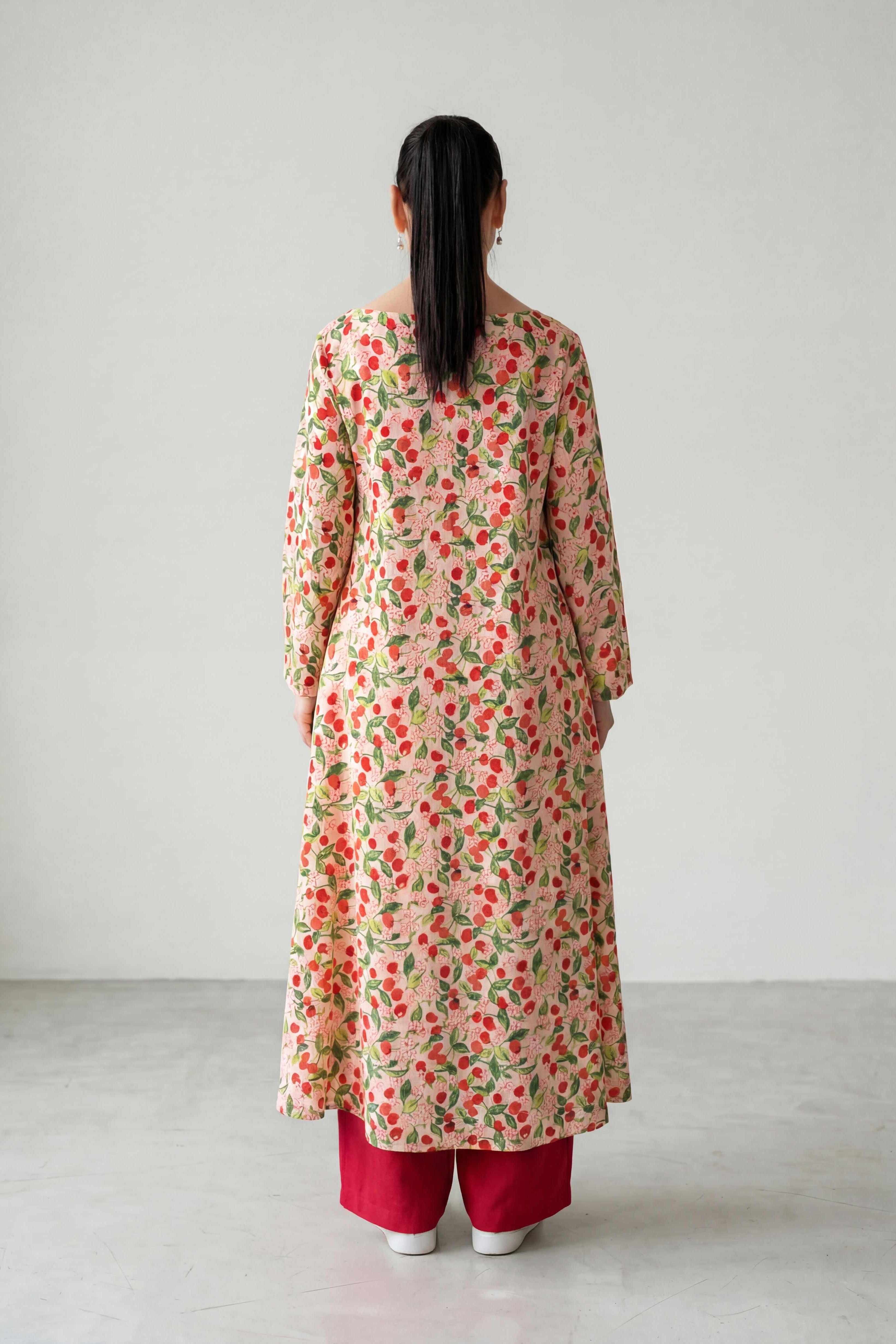 Person wearing a floral long coat and red pants on a plain background