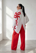 Woman wearing a white top with red floral patterns and red pants in a bright room.