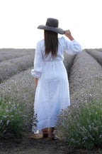 Woman in a white dress and wide-brimmed hat walking through a lavender field.