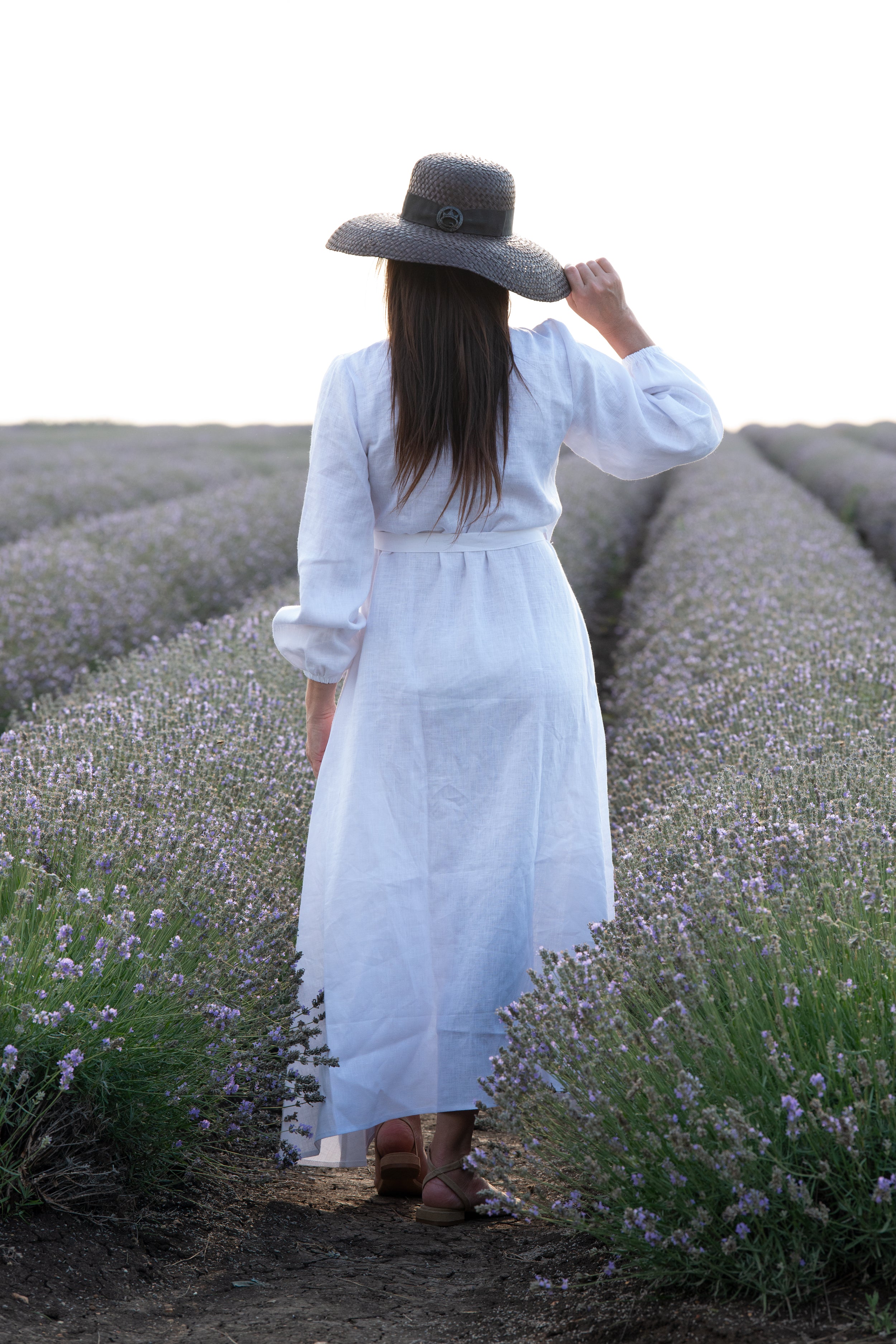 Woman in a white dress and wide-brimmed hat walking through a lavender field.