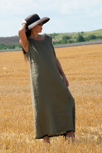 Woman in a long green linen dress and black hat standing in a wheat field.