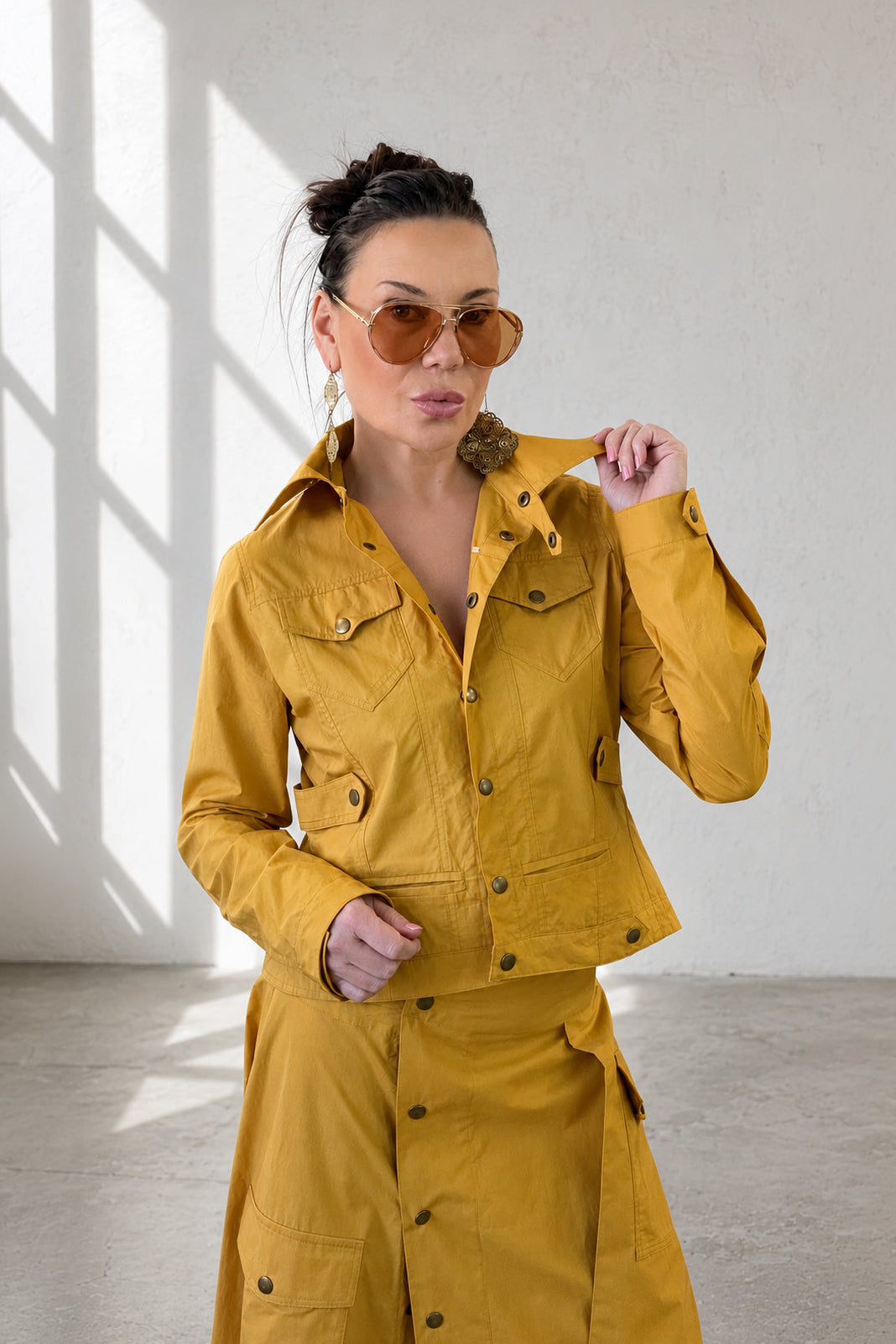 Woman wearing a mustard yellow outfit with sunglasses in a bright room.