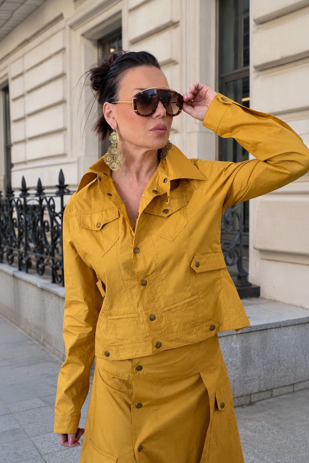 Woman in a mustard yellow jacket standing on a street with a building in the background