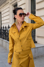 Woman in a mustard yellow jacket standing on a street with a building in the background