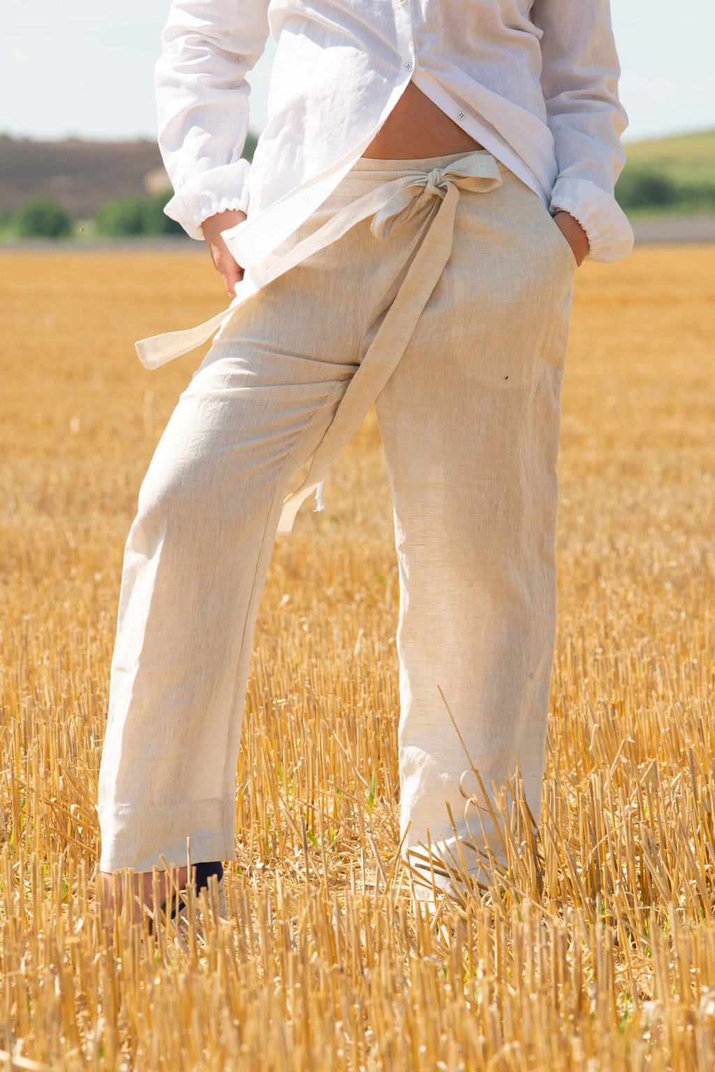 Person wearing light-colored pants and a white shirt standing in a field of tall grass.