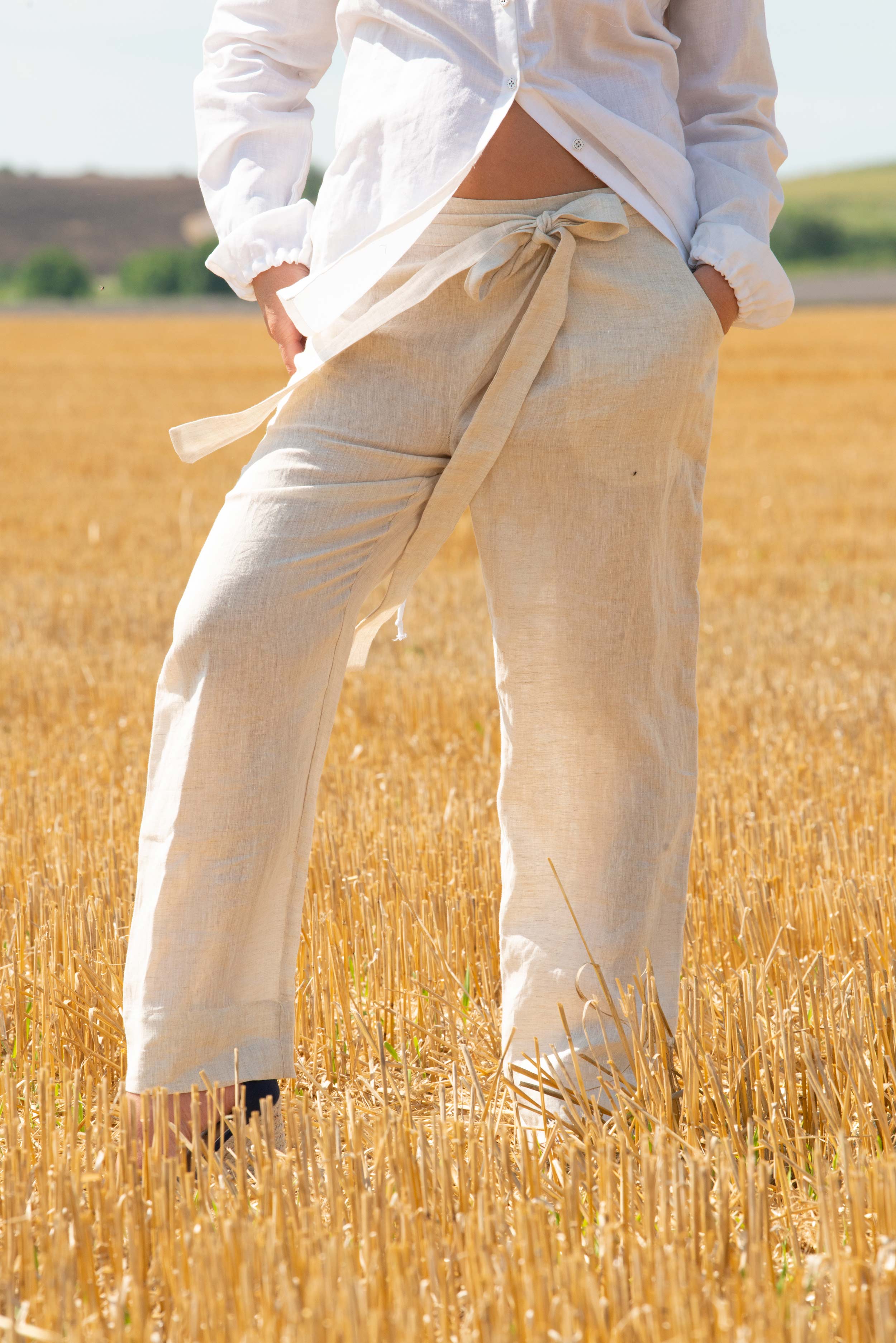 Person wearing light-colored pants and a white shirt standing in a field of tall grass.