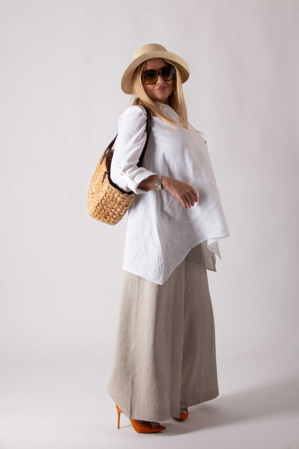 Woman wearing a white shirt, beige wide-leg pants, and a straw hat with a white background
