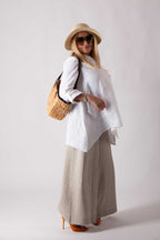 Woman wearing a white shirt, beige wide-leg pants, and a straw hat with a white background