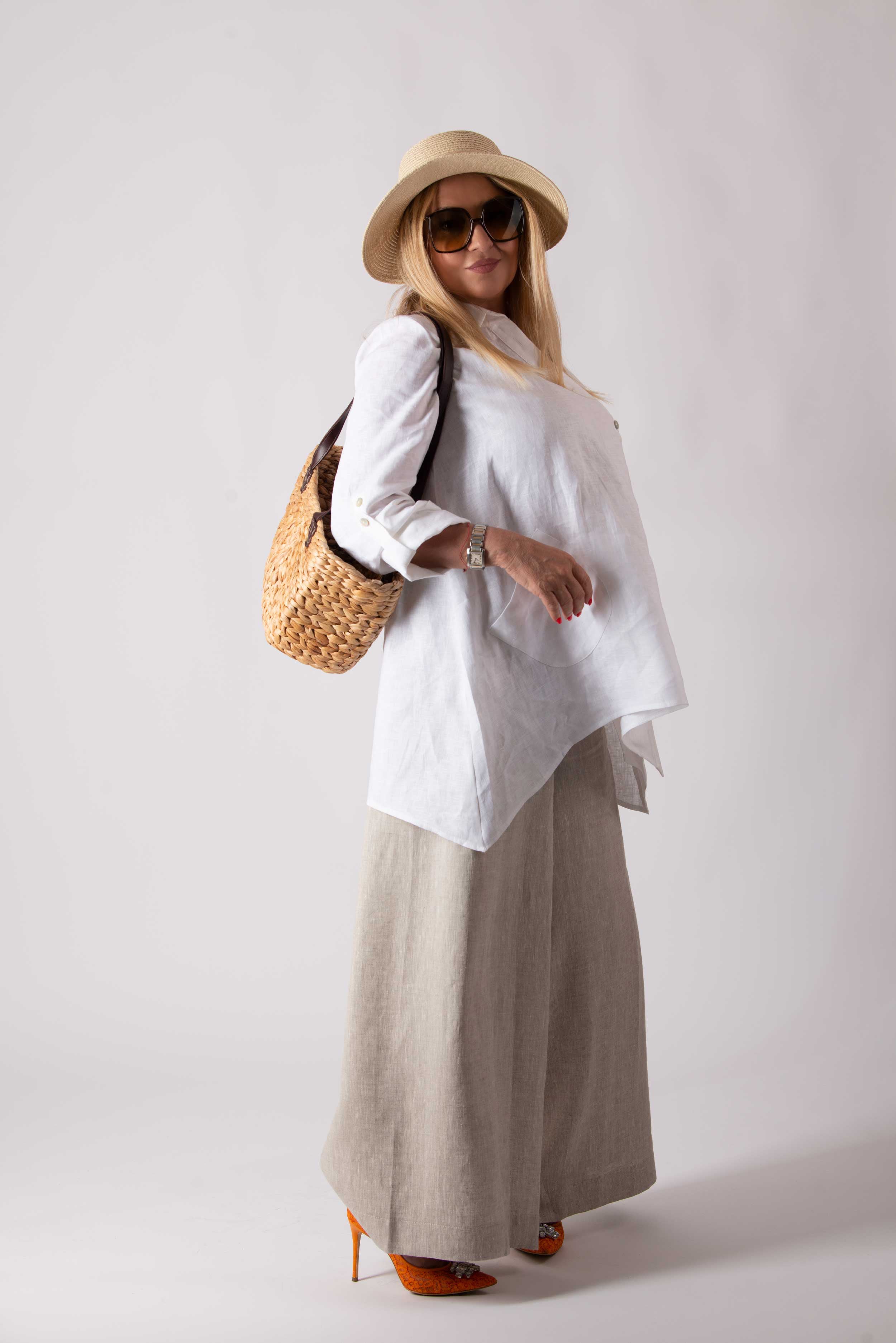 Woman wearing a white shirt, beige wide-leg pants, and a straw hat with a white background