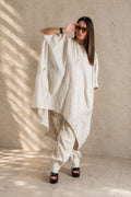 Woman wearing a loose-fitting natural linen outfit against a textured wall.