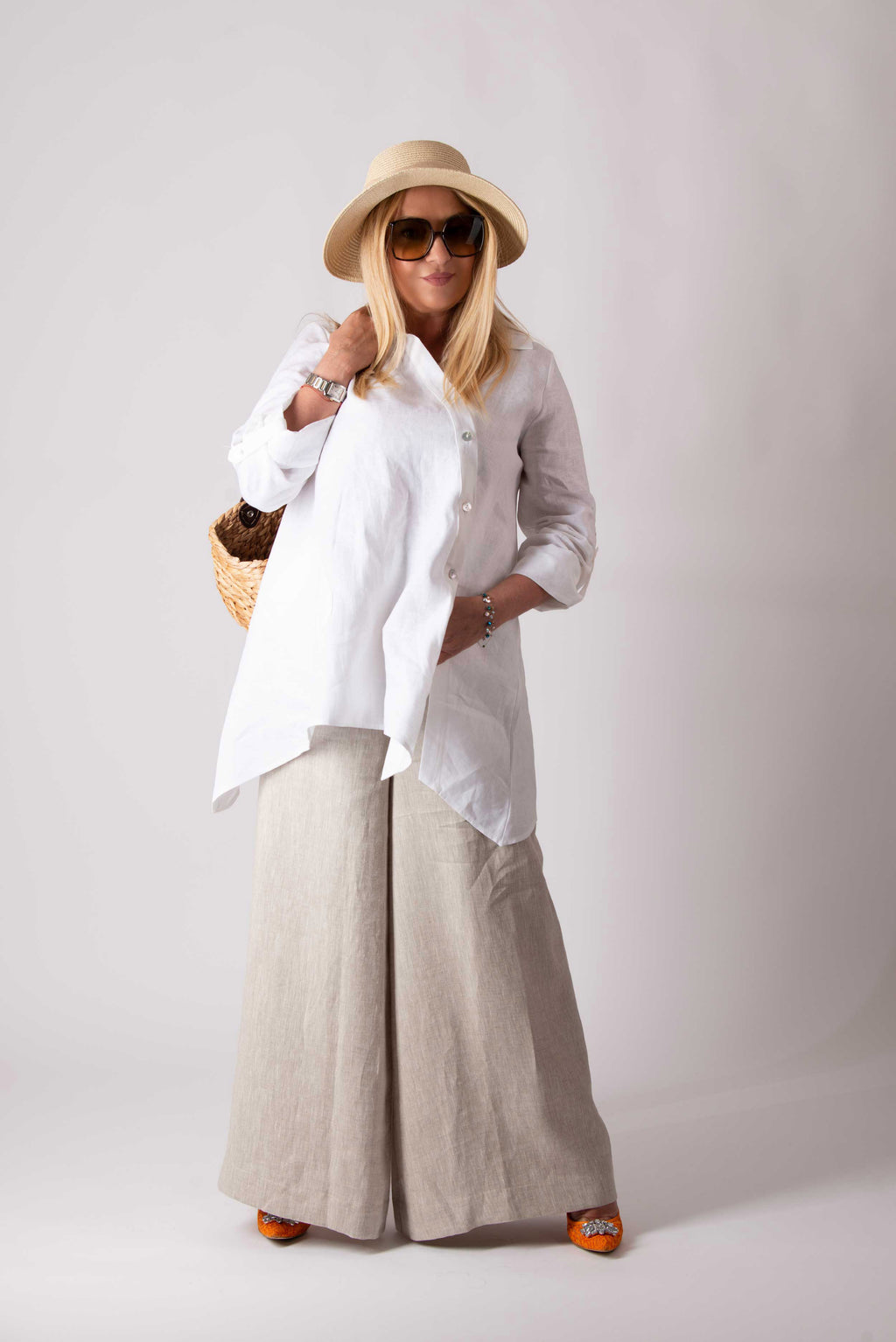 Woman wearing a white shirt, beige wide-leg pants, and a straw hat on a plain background