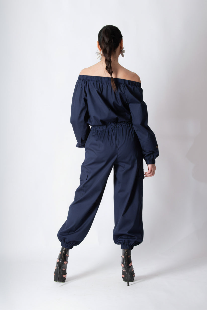 Person wearing a navy blue off-shoulder jumpsuit on a white background