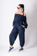 Woman wearing a navy off-shoulder jumpsuit with matching sneakers on a white background