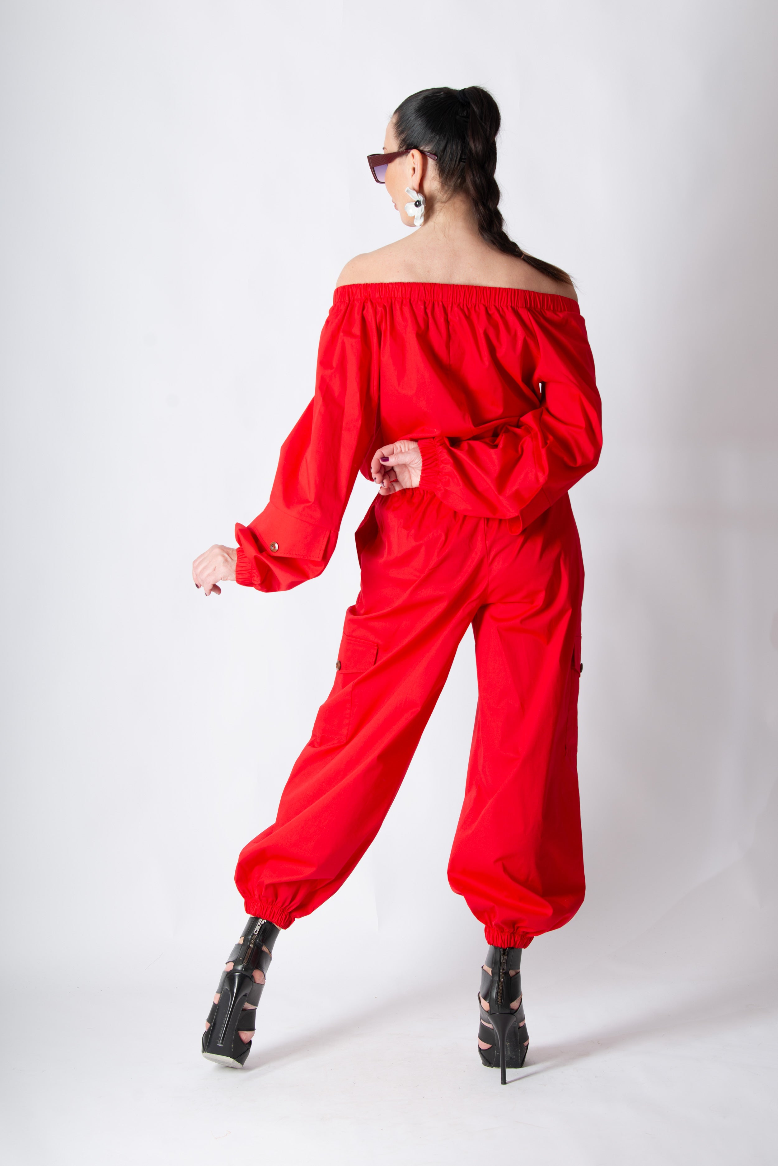 Person wearing a red off-shoulder jumpsuit on a white background