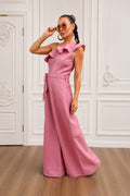 Woman wearing a pink jumpsuit in a room with white walls and wooden floor.