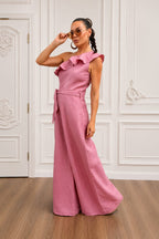 Woman wearing a pink jumpsuit in a room with white walls and wooden floor.