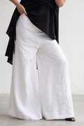 Person wearing a black top and white wide-leg pants on a blurred street background