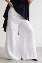 Person wearing a black top and white wide-leg pants on a blurred street background