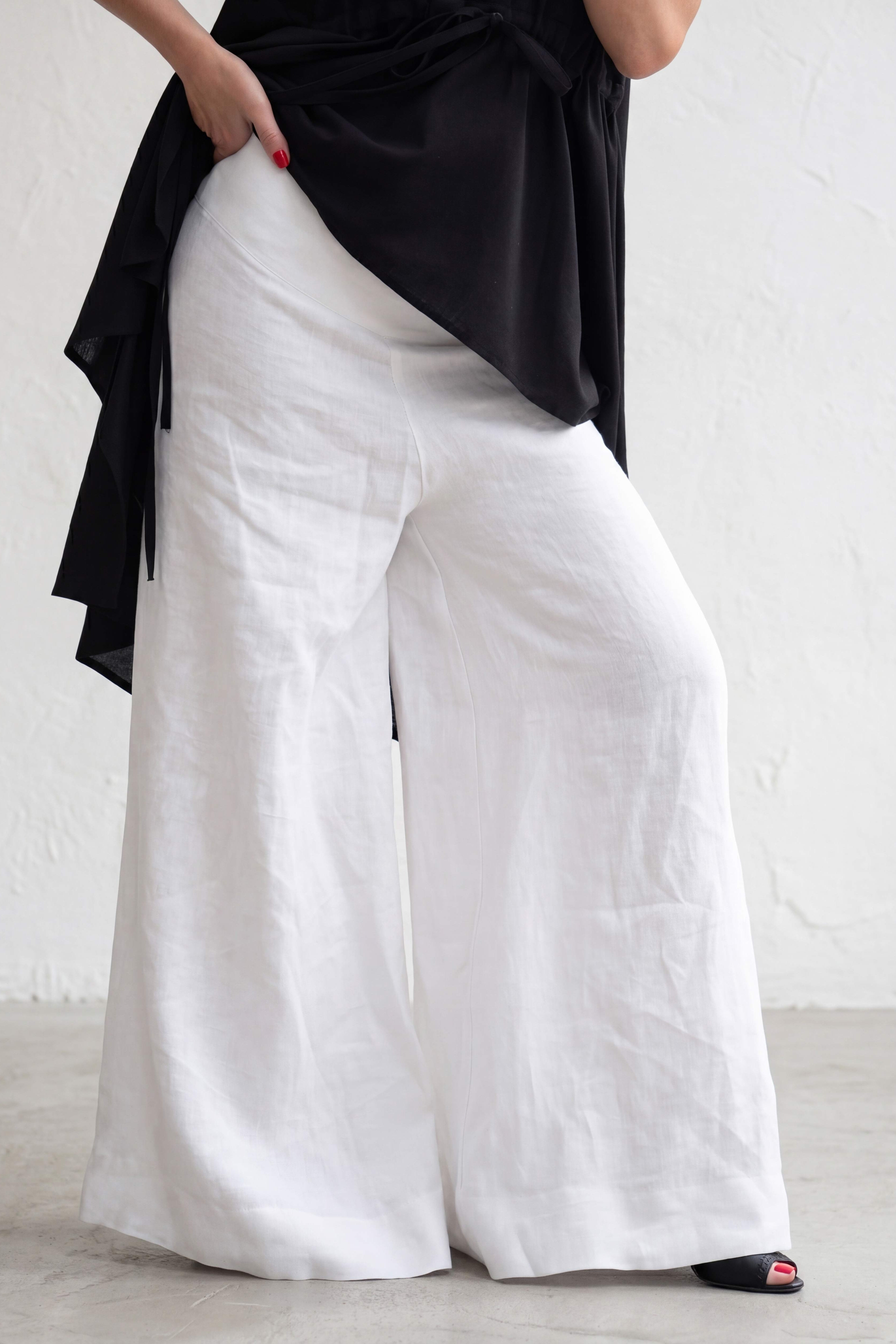 Person wearing a black top and white wide-leg pants on a blurred street background